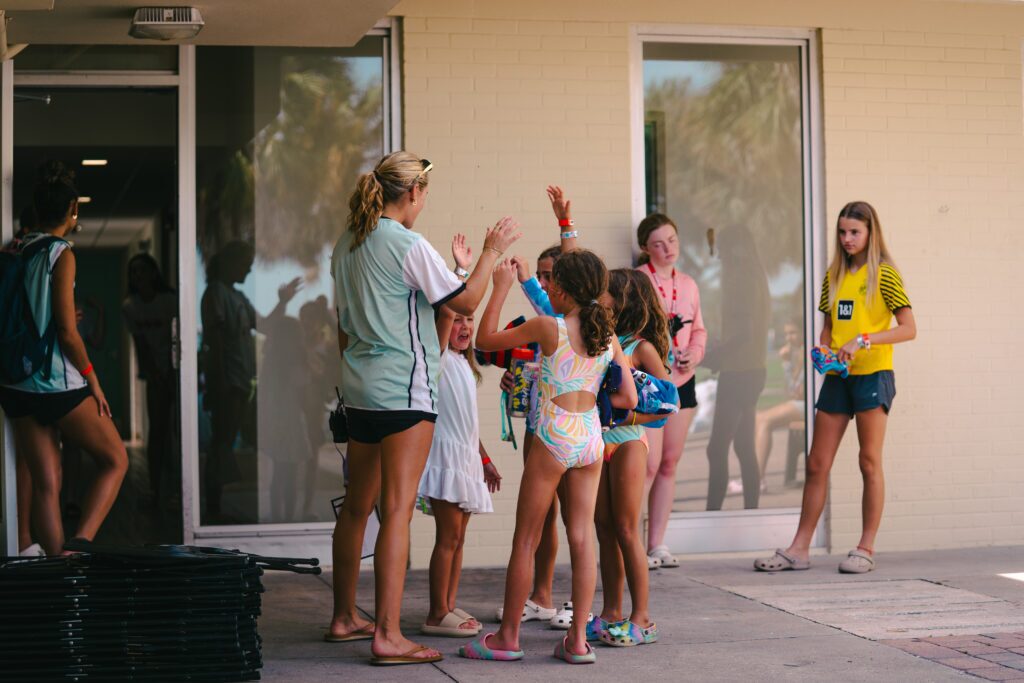 Parents and campers checking in at Signature Sports Camps, greeted by friendly and caring staff during summer camp arrival ampers raising their hands to answer swim orientation questions from a coach at Signature Sports Camps