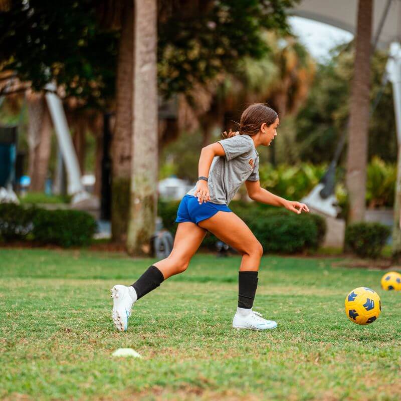 Girl running after soccer ball during practice at sports camp