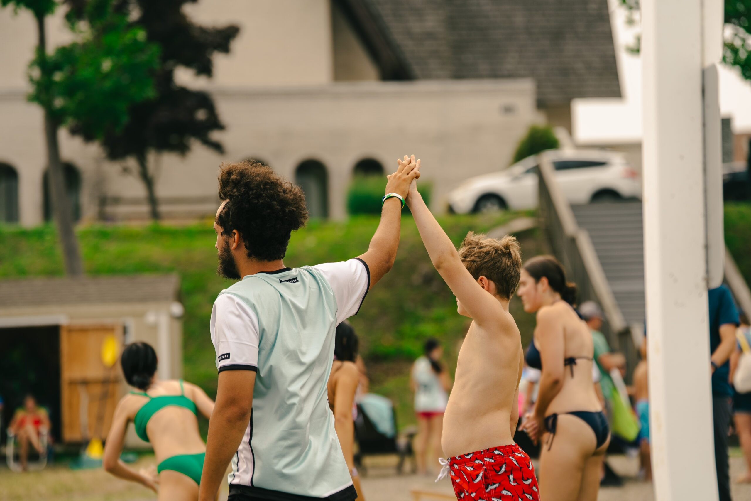 Group of people in swimsuits at an outdoor pool, raising hands in celebration.