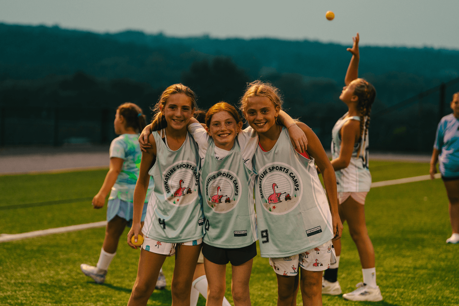 Three girls wearing Signature Sports Camps uniforms smile for a photo after lacrosse practice