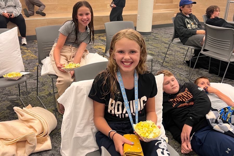 Kids at summer camp sitting with popcorn watching a movie