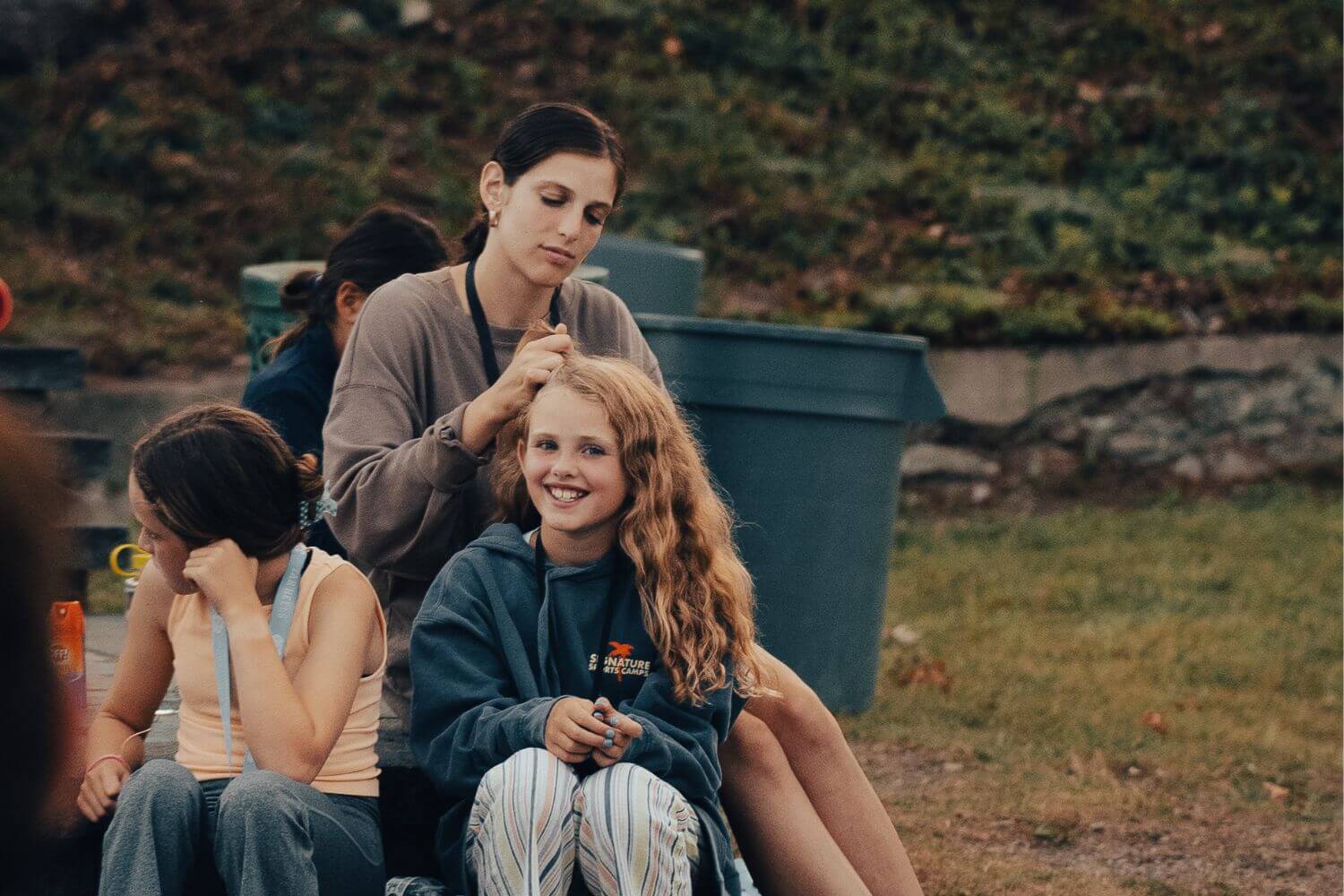 A young camper is getting her hair braided by a counselor during break time at camp