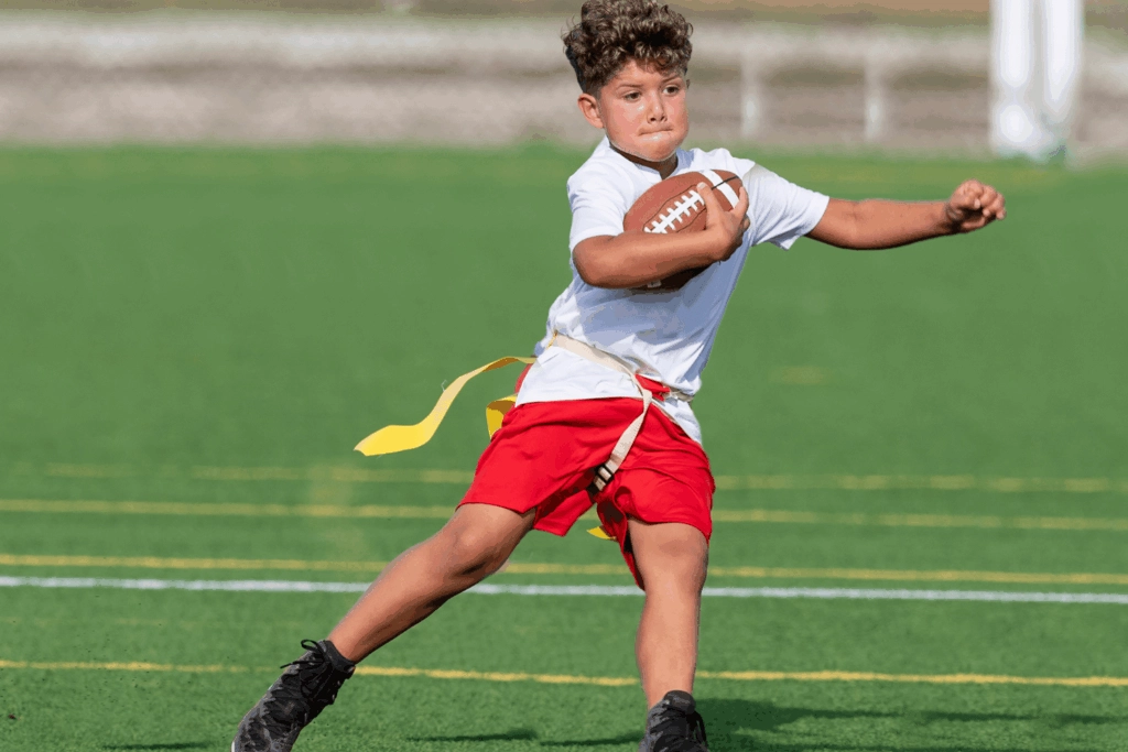 Boy in red shorts and white shirt with yellow football flag holding a football