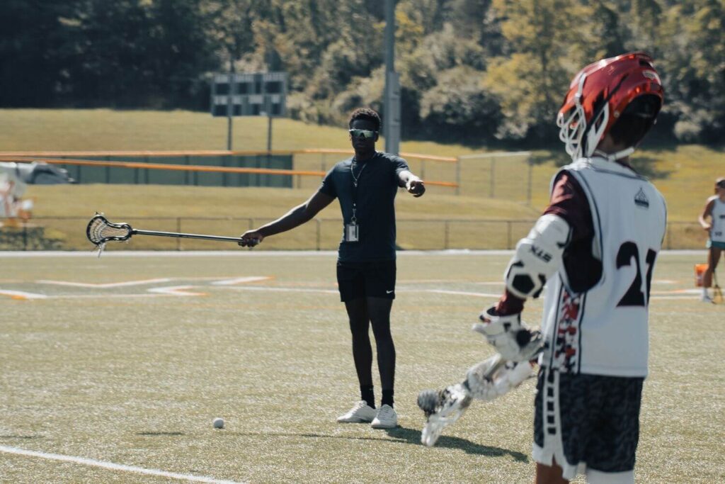 A coach at signature sports camps is giving instruction to a young lacrosse player during camp