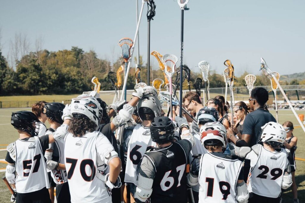A group of co-ed youth lacrosse players huddling after a practice session at overnight sports camp