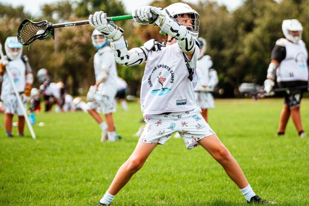 A lacrosse player wearing Signature Sports Camp uniform is in action during a lacrosse scrimmage