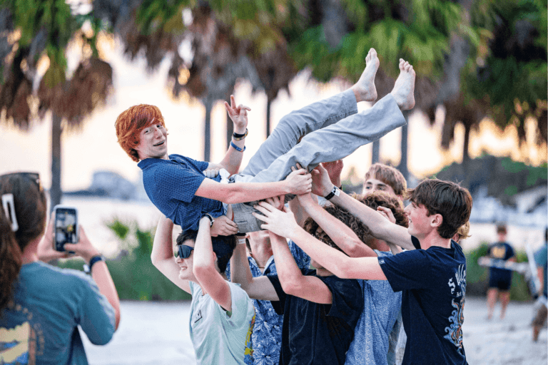 A group of kids holding their friend up in the air during a beach party at overnight sports camp in Florida