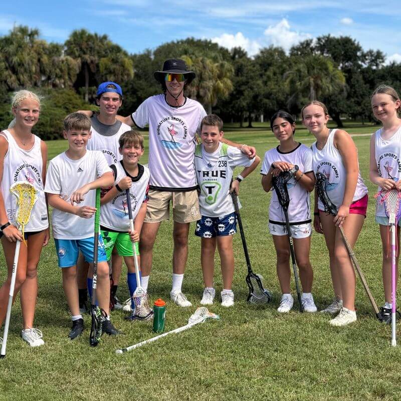 A group of campers pose with their coach after lacrosse practice
