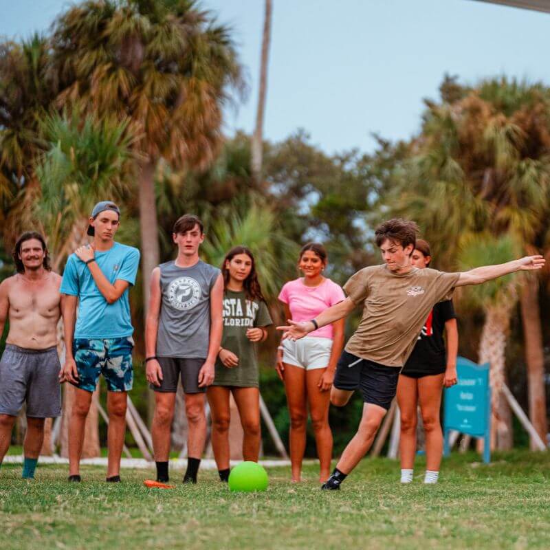 Boy kicking a green ball during a camp game of kickball