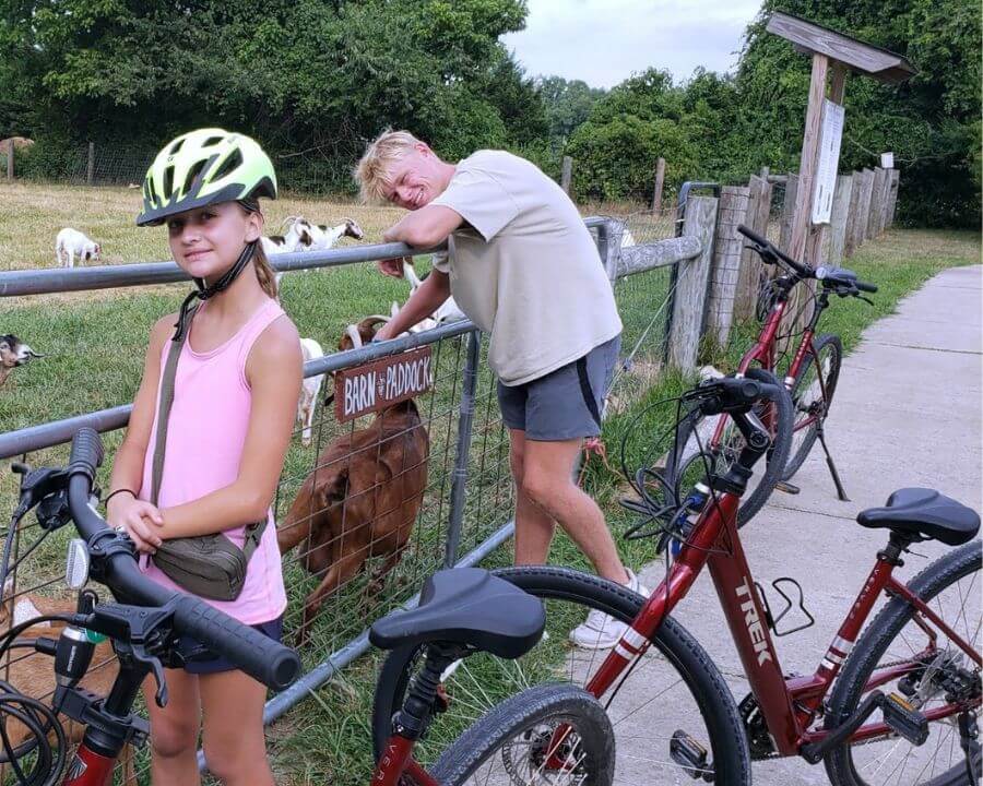 A boy and girl are standing next to a barn with bikes while on an adventure at overnight summer camp