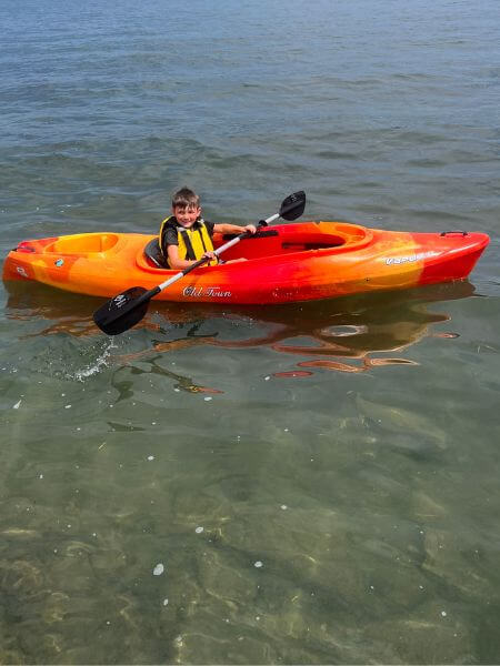 A young boy wearing a yellow life jacket in a kayak on the lake