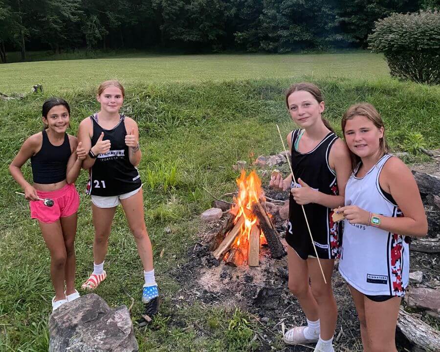 Four girls at Lacrosse camp are standing next to a campfire with smores