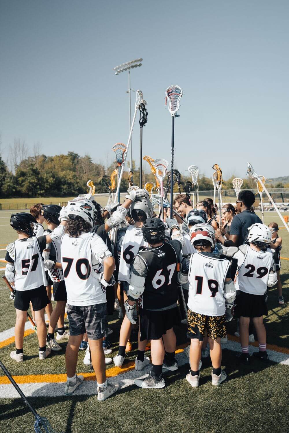 A Lacrosse team standing together in a huddle with their sticks pointed towards the sky