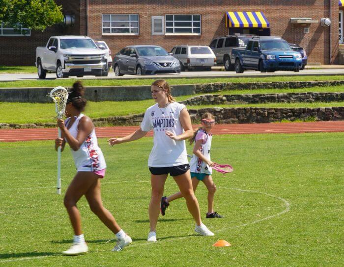 Professional Lacrosse player Izzy Scane is coaching a young lacrosse athlete during summer camp