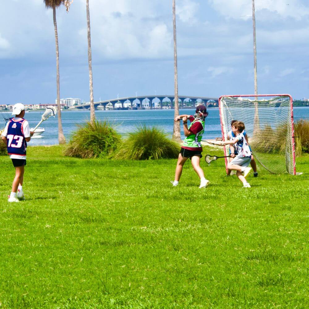 A group of young male lacrosse players engaged in a game on a field overlooking the water in Florida