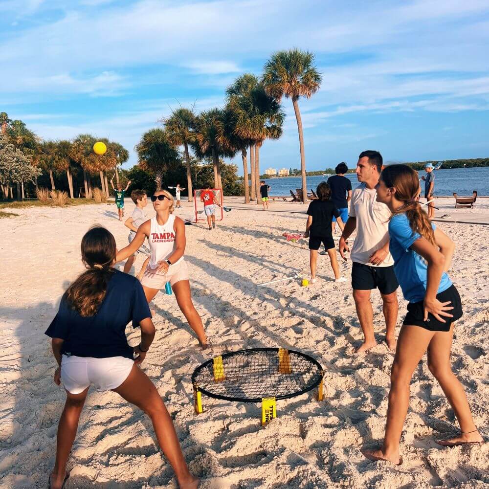 Lacrosse camp coaches and campers are playing a game of Spikeball on the sand at the beach in Florida