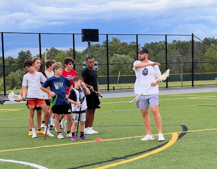 Professional Lacrosse player Izzy Scane is coaching a young lacrosse athlete during summer camp