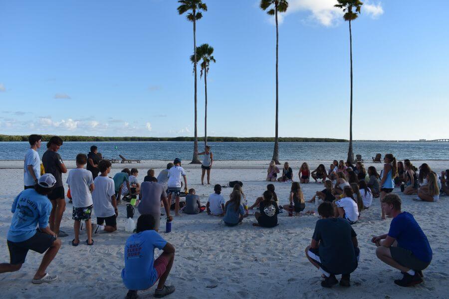 A group of lacrosse campers gathered on the beach while listening to the camp director