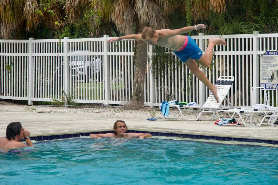 A boy doing a bellyflop into a swimming pool as his friends look on