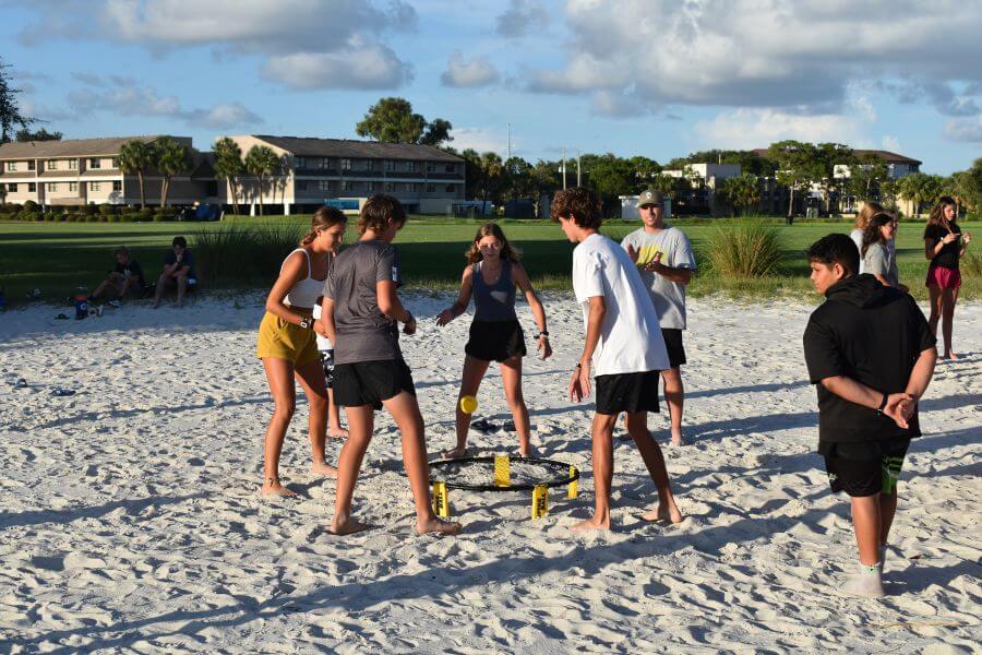 Lacrosse players playing a game of spikeball at camp on the beach