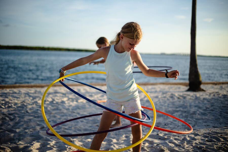 A young girl is hula-hooping on the beach with four different colored hoops