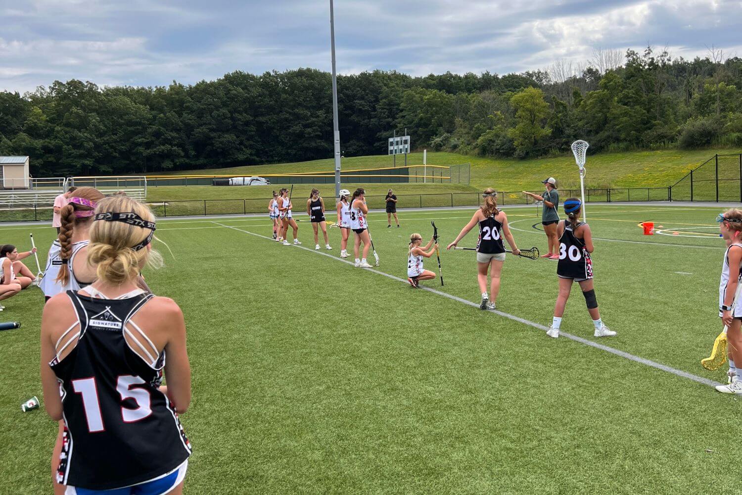 Female lacrosse players receiving instruction from a professional lacrosse player during camp