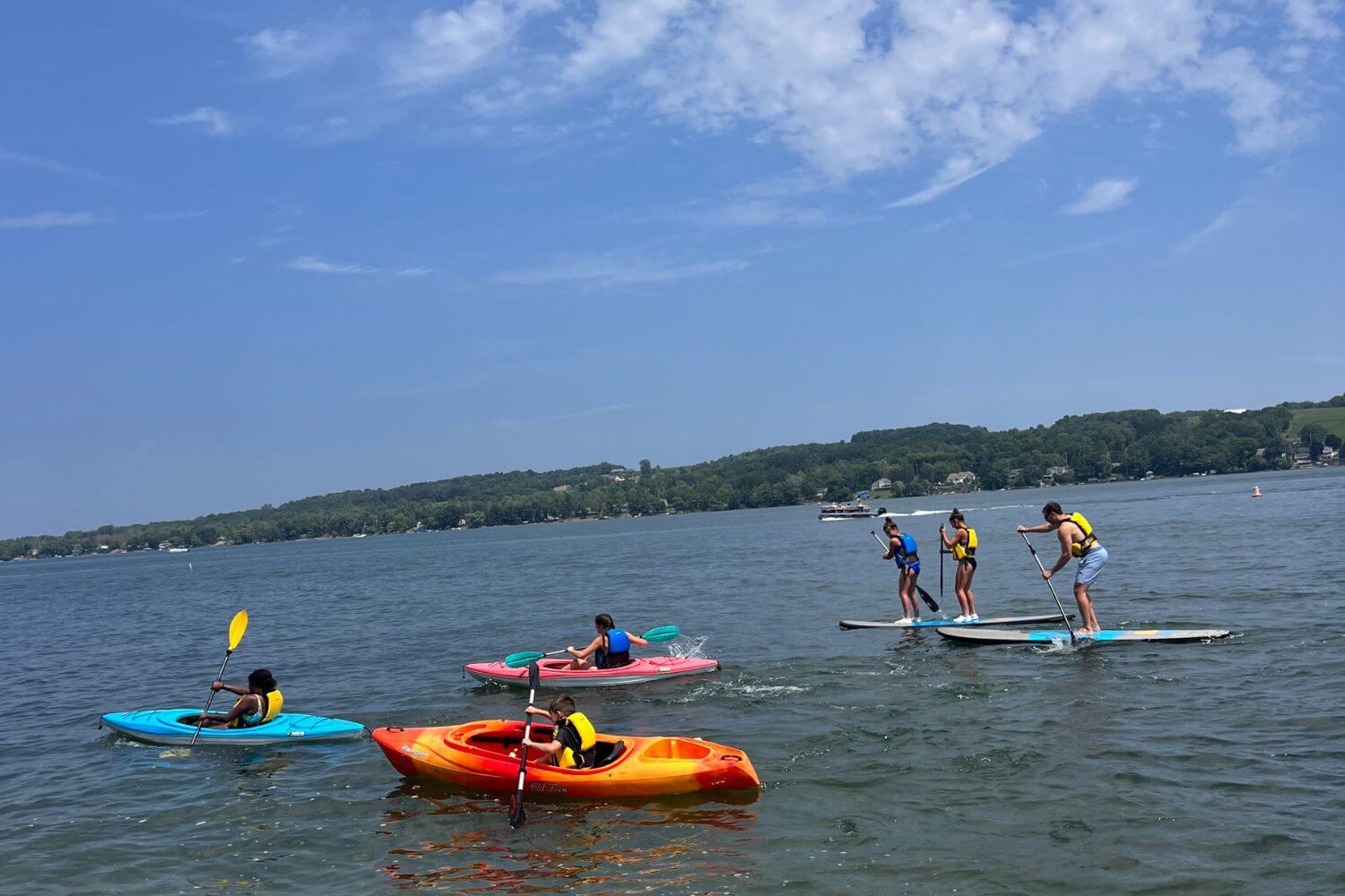 Summer campers on stand up paddleboards and kayaks having fun on the lake