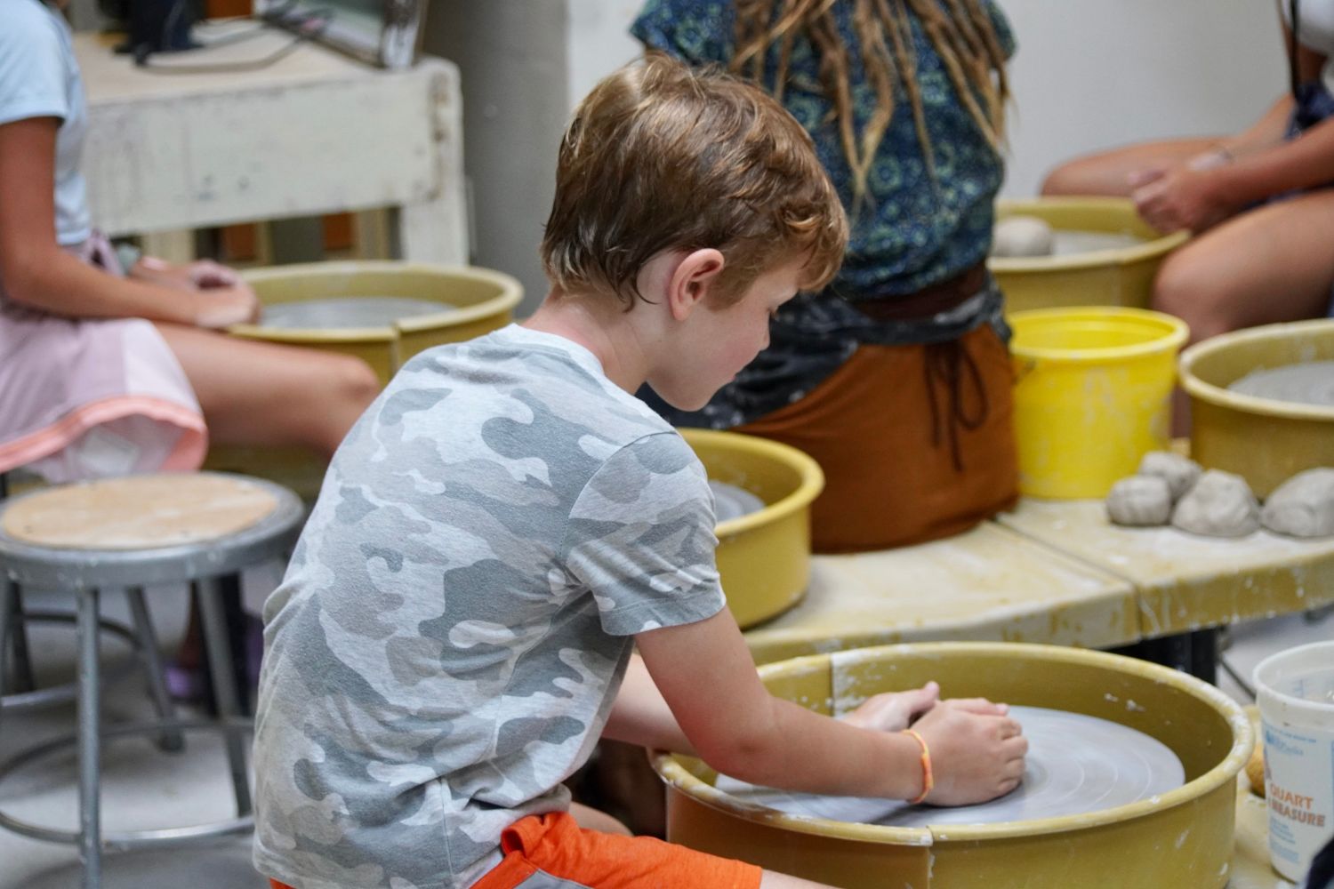 A young boy sitting at a pottery wheel during activity time at overnight sports camp