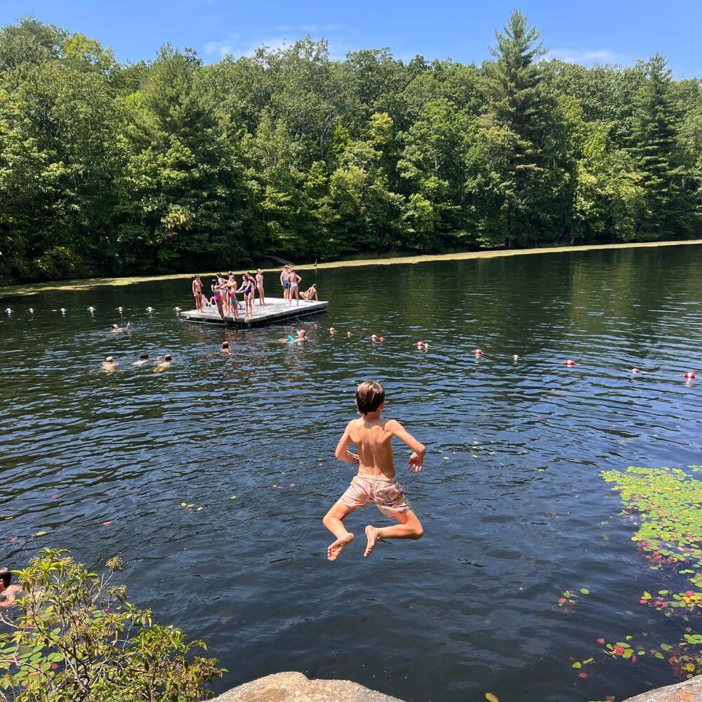 A young boy jumping into a lake as his friends watch on from the water at overnight summer camp in Tennessee