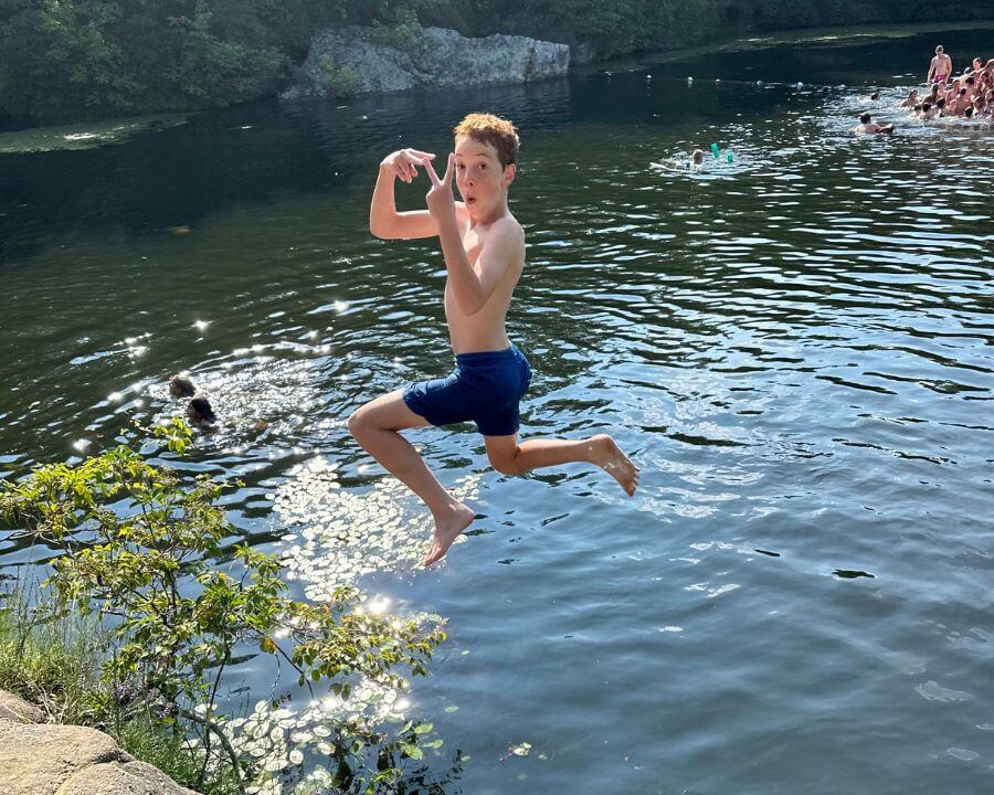 A young boy is jumping into a watering hole, holding up the peace sign as he jumps in