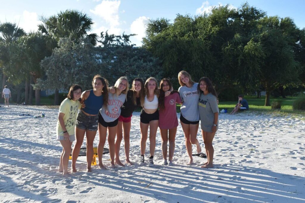 8 girls are locked arms while standing on the beach at lacrosse summer camp