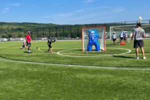 Young lacrosse player is being instructed by two sports camp coaches during outdoor practice