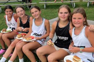 Group of girls at overnight sports camp enjoying camp BBQ and fresh fruit