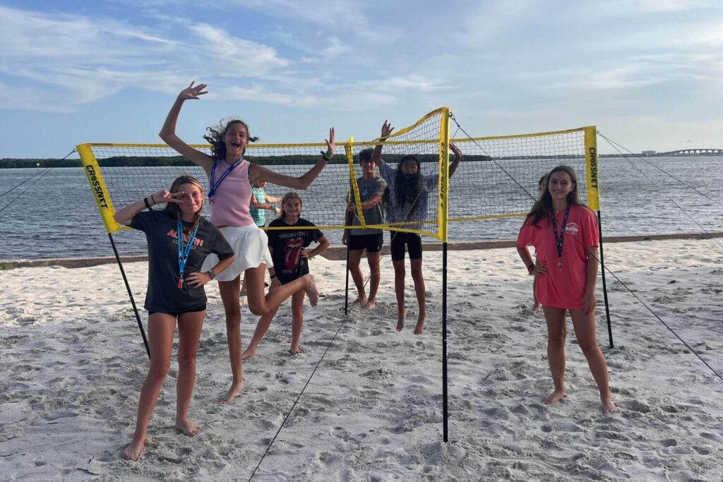 Kids at overnight sports camp posing for a silly picture while playing volleyball on the beach