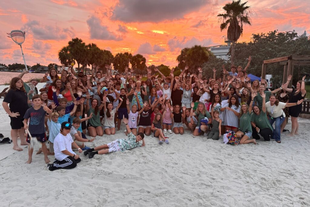 A group of athletes at sports camp smile for a photo on the beach at sunset