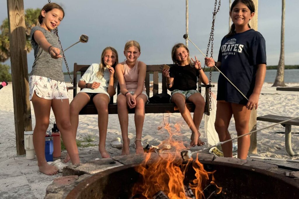 five girls at overnight sports camp roasting marshmallows by the fire on the beach