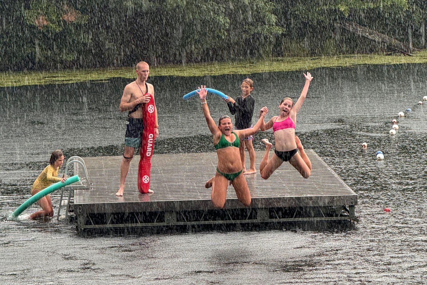 Girls holding hands as they jump into the lake on a rainy day