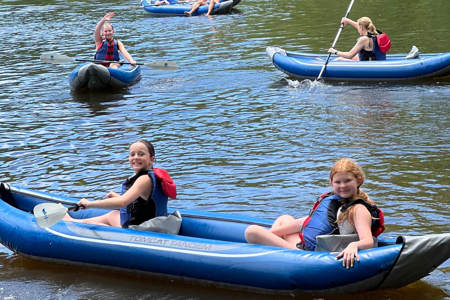 Two girls wearing lifejackets are posing for a photo while in a blue kayak