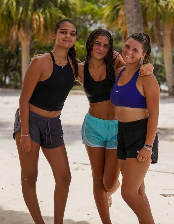 Three girls locked arms for a photo on the beach at sports camp