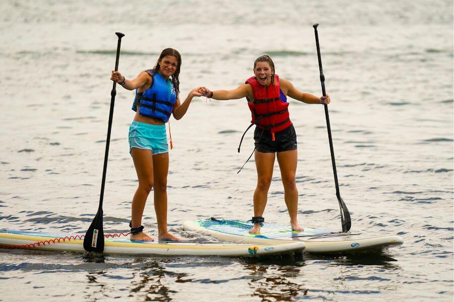 Two girls on stand up paddleboards smile for a photo