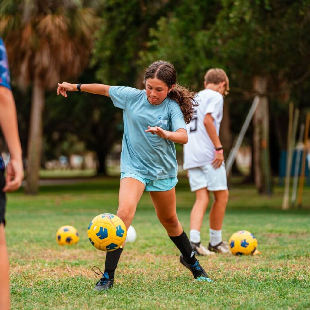 Girl wearing blue soccer jersey dribbling soccer ball at sports camp