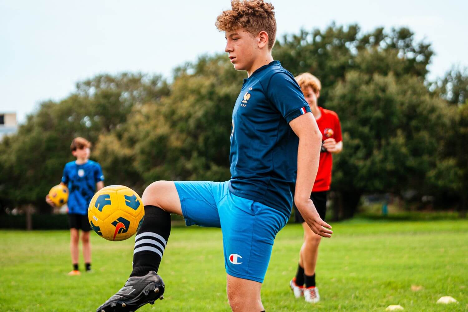 Boy in blue shirt and shorts dribbling a yellow soccer ball