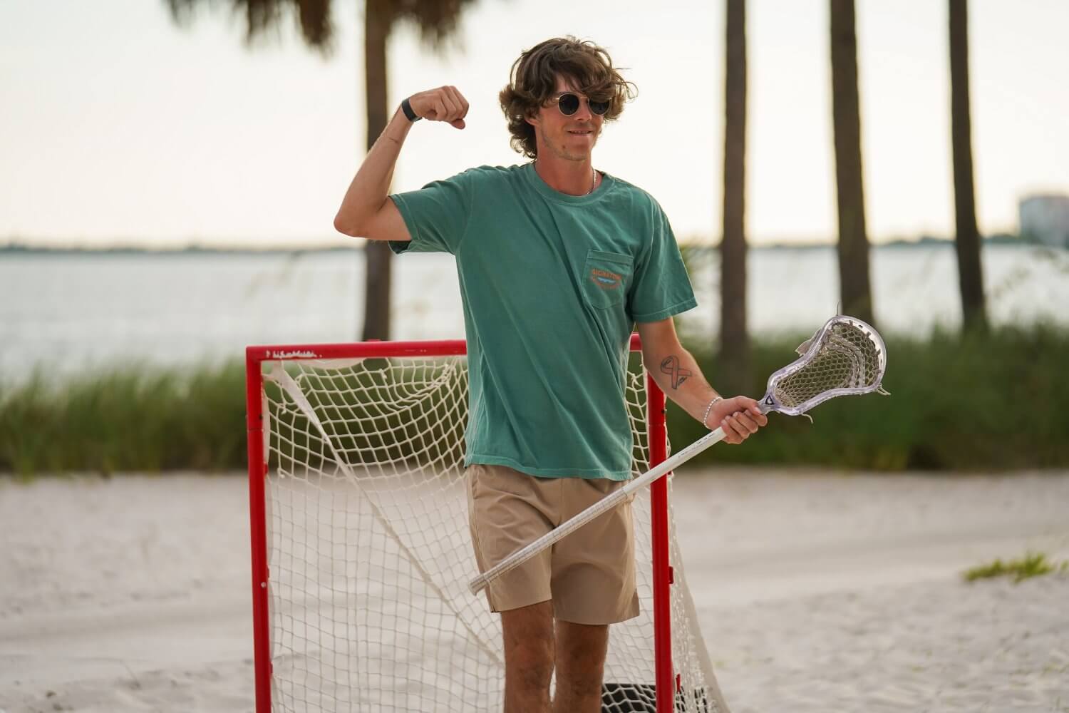 Coach wearing a green shirt holding a lacrosse stick on the beach