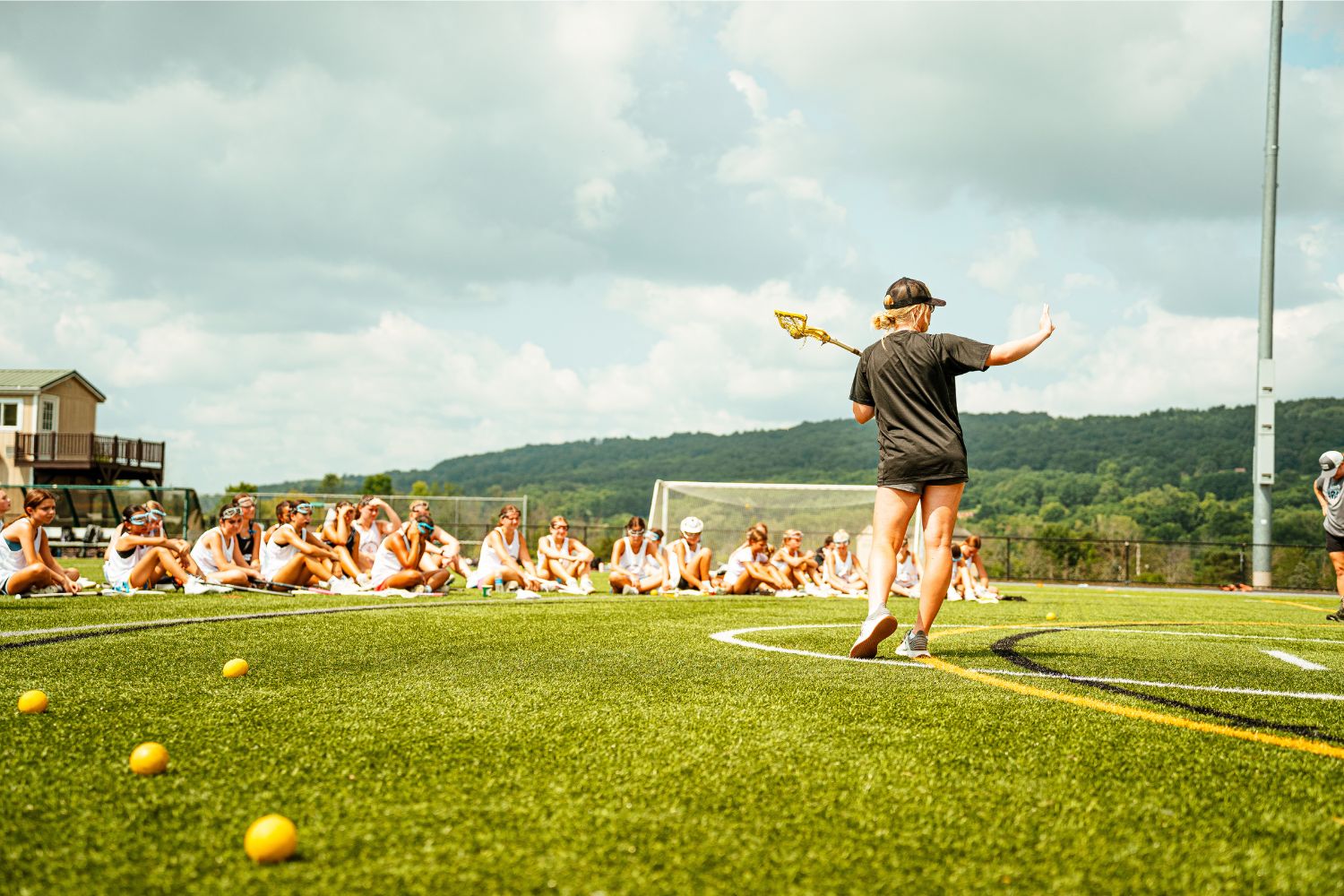 Lacrosse athletes sit on a field as a coach is giving direction