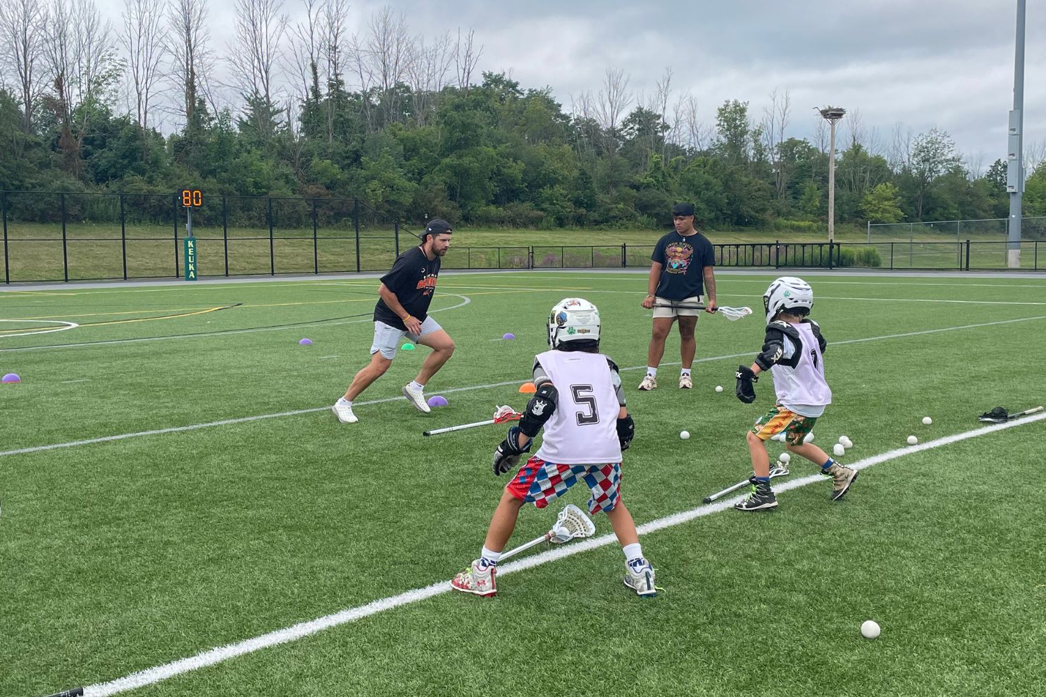 Two coaches and two lacrosse players are practicing drills