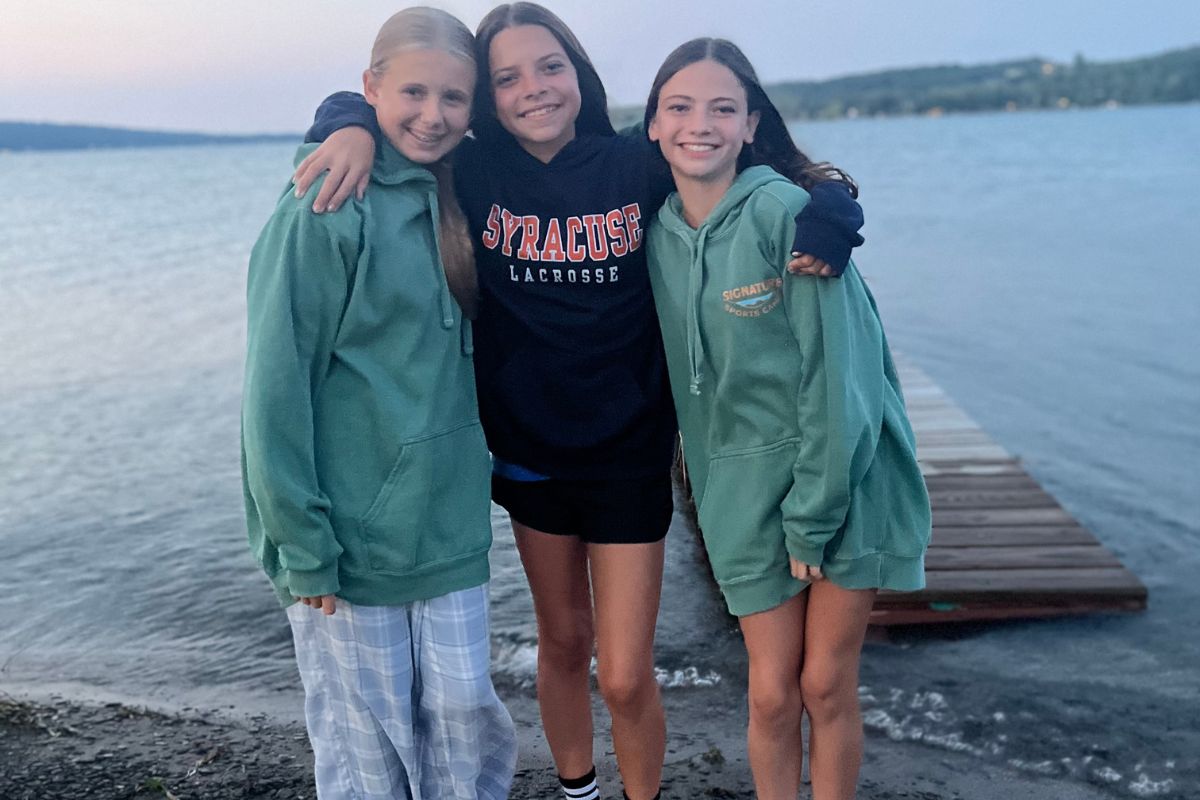 Three girls in sweaters pose together for a photo by the lake