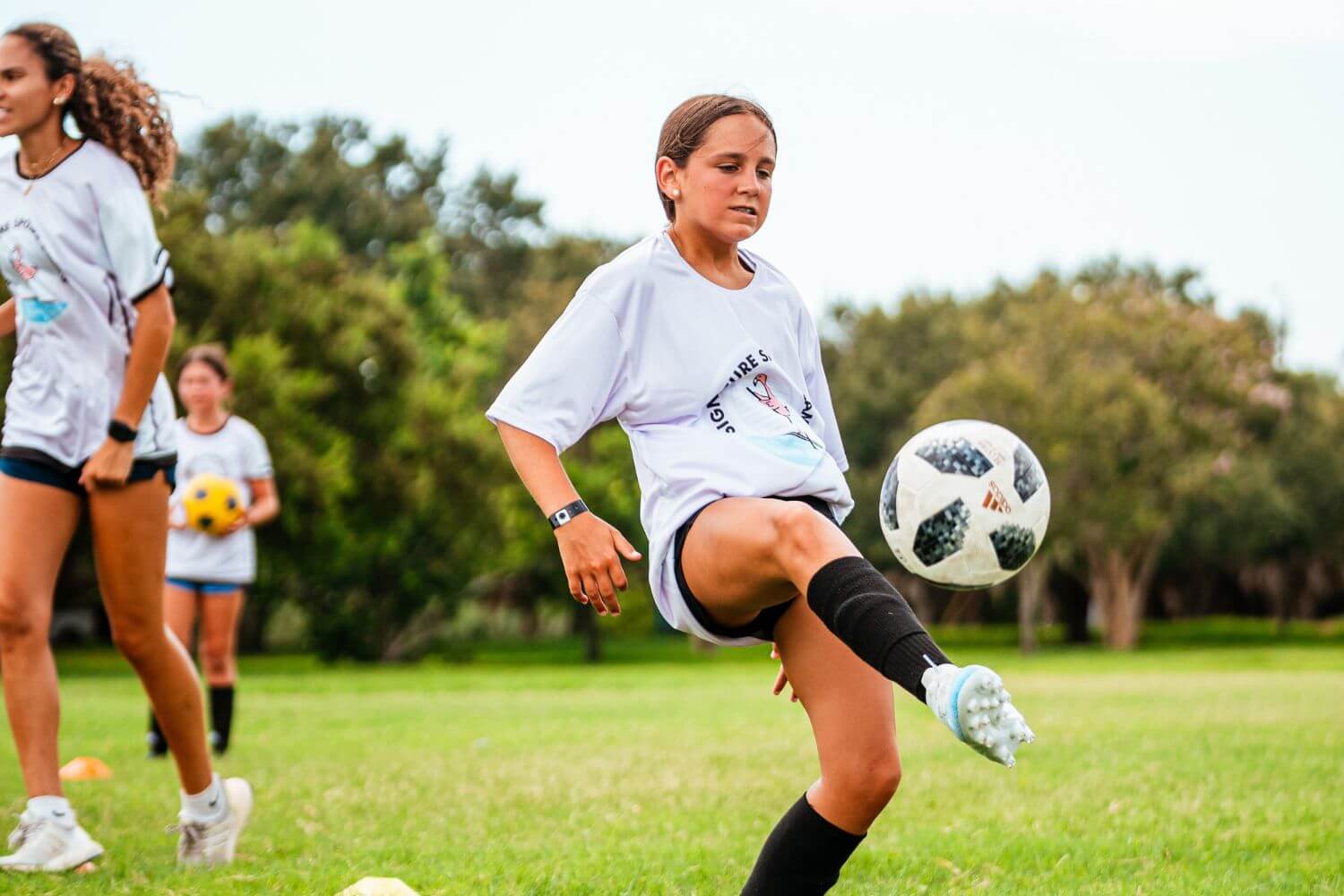 Girl at sports camp dribbling a white soccer ball