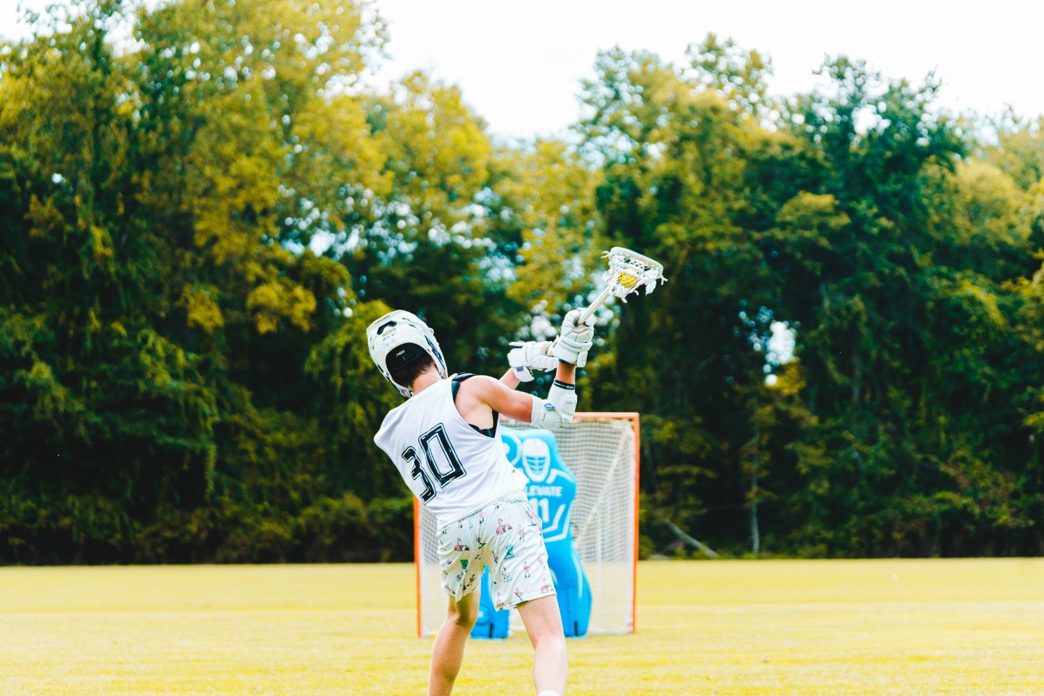 Boy wearing lacrosse gear on the field taking goal shots at practice