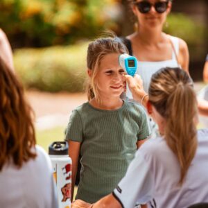 A camp counselor is taking the temperature of a new camper at registration check in