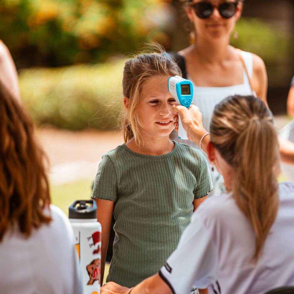 A camp counselor is taking the temperature of a new camper at registration check in